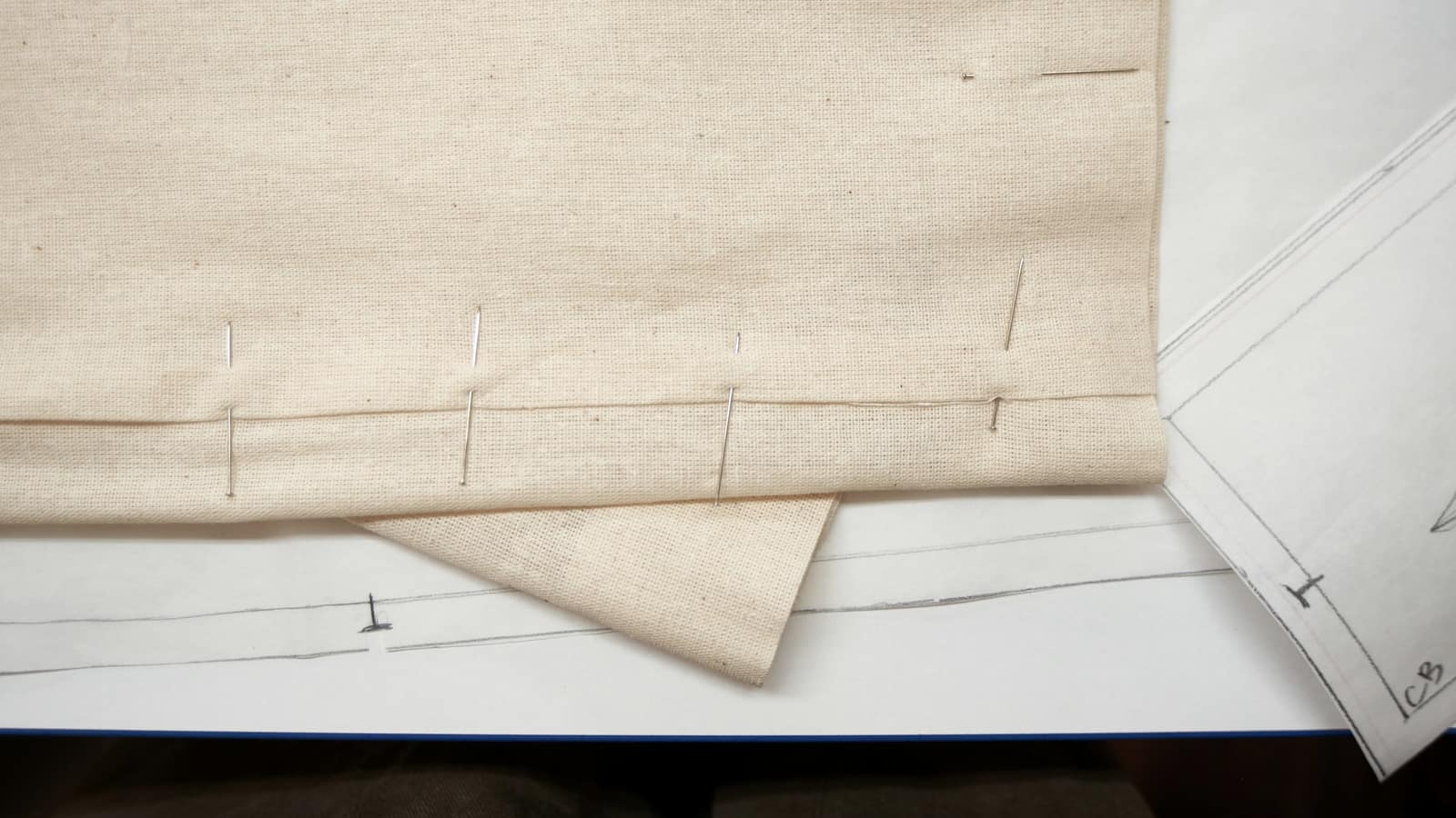 Calico pinned along a seam line over a drafted paper pattern
