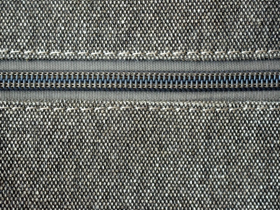A coil zipper set into woven fabric with white top stitching, close crop