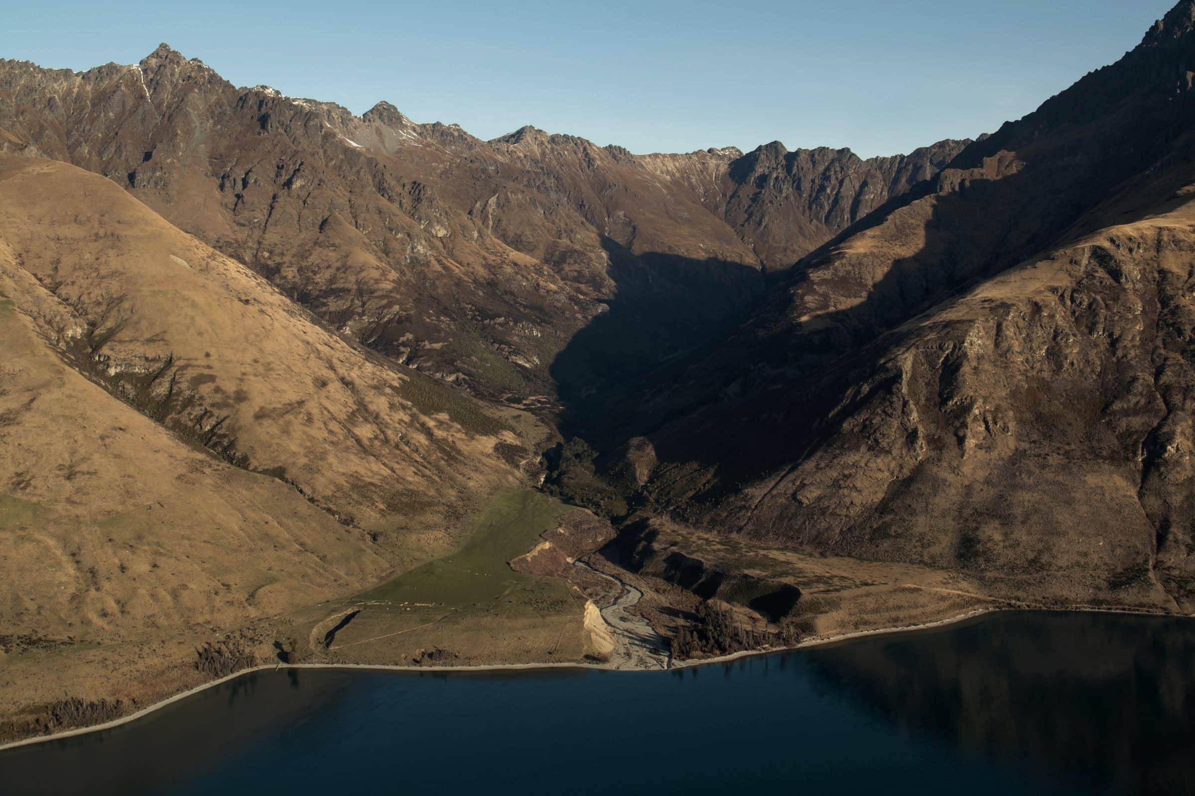 Rugged brown ridges dropping to dark lake water near Queenstown, New Zealand