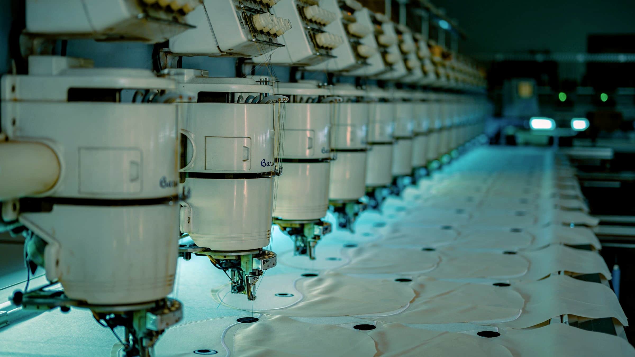 A row of industrial embroidery machine heads in cool available light