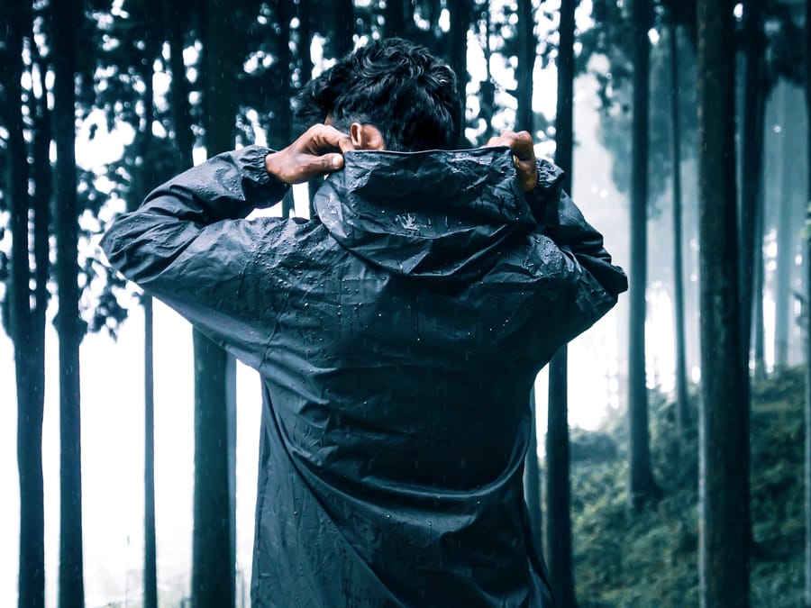 Hands pulling up the hood of a wet technical shell, seams visible