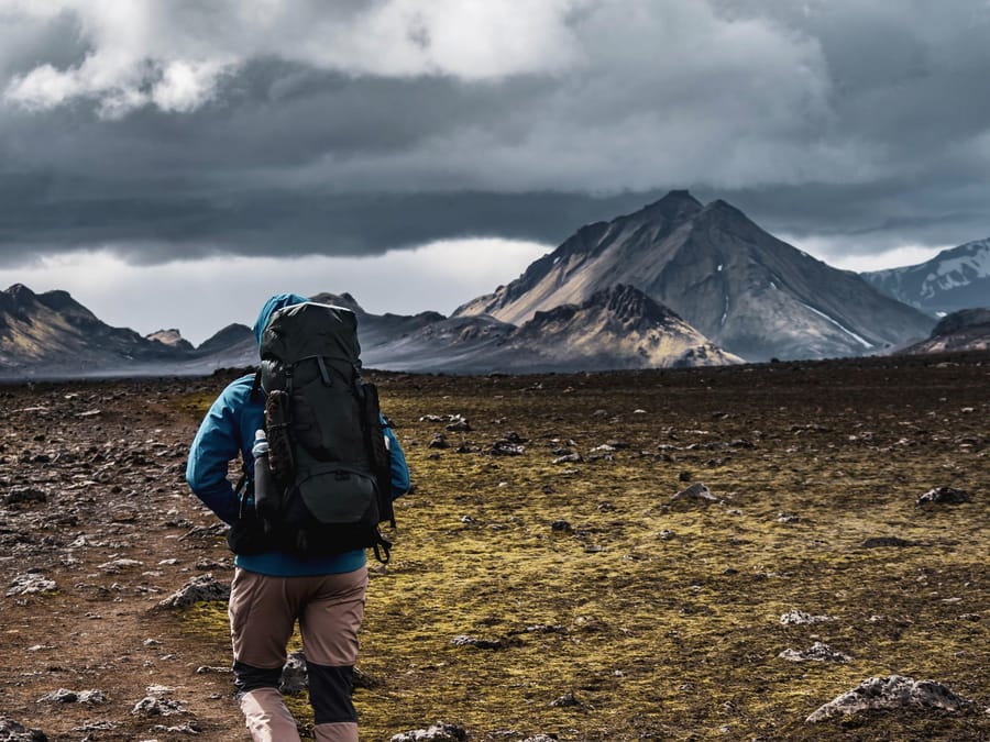 A hiker under a full pack walking toward grey peaks, Laugavegur, Iceland
