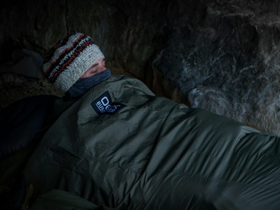 Someone asleep in a sleeping bag under a rock overhang